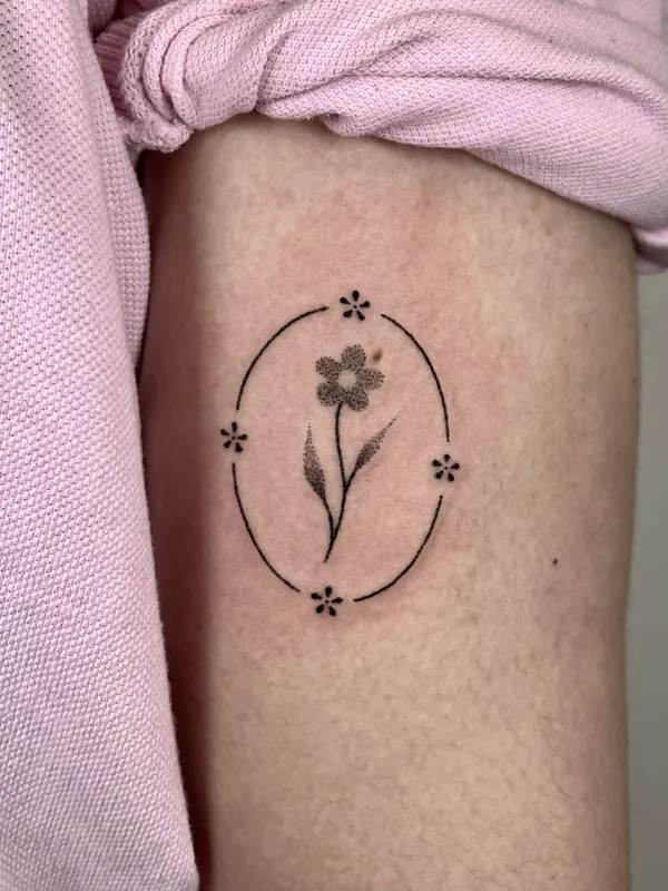 Fine line flower framed in an oval, hand-poked on the thigh