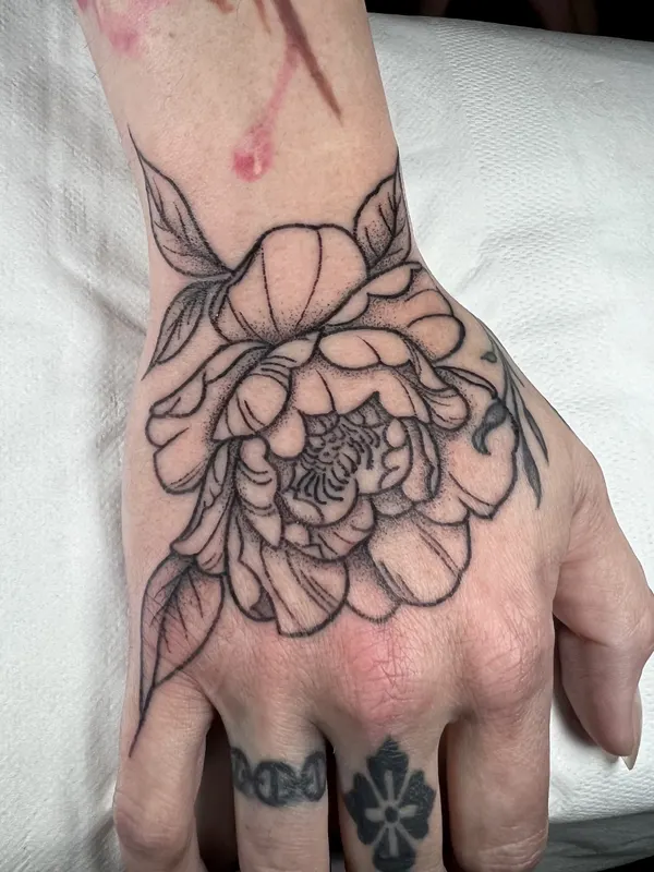Fine line peony hand-poked across the back of the hand