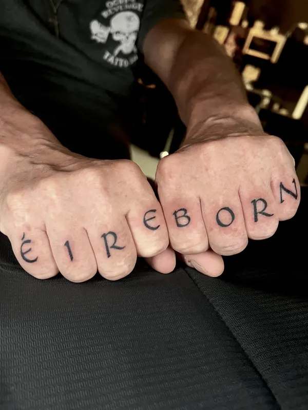 Hand-poked lettering across the knuckles reading ÉIRE BORN