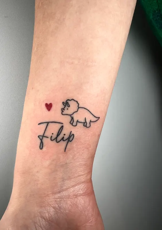 Hand-poked script reading Filip with a small dinosaur and red heart on the wrist
